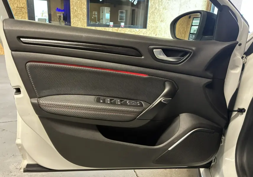 Vue intérieure de la porte avant droite blanche d'une Renault Mégane IV RS 280 avec surpiqûres rouges et insert carbone.