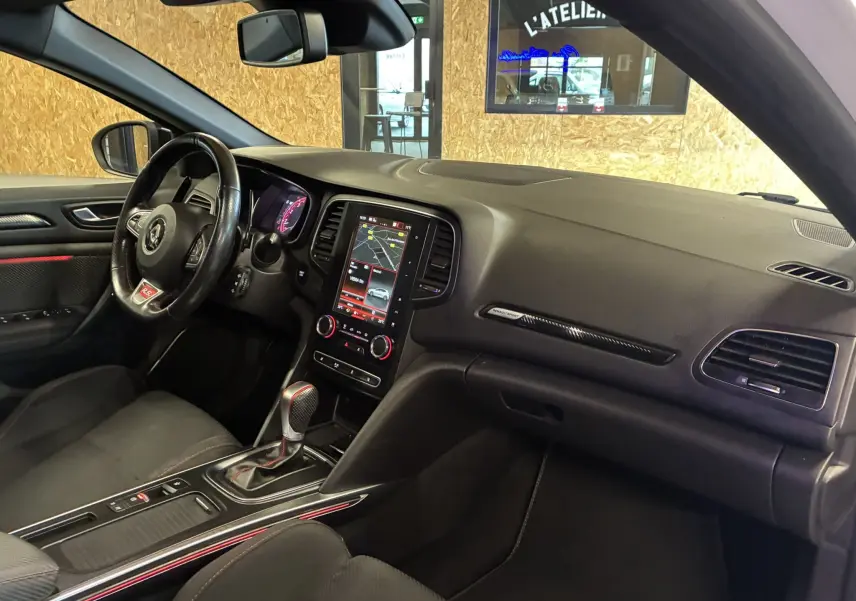 Vue intérieure côté conducteur de la Renault Mégane IV RS 280 EDC6 avec tableau de bord noir et écran tactile central allumé.