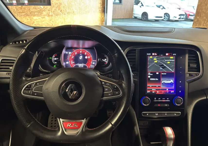 Vue intérieure centrée sur le volant noir R.S. et l’écran tactile du tableau de bord de la Renault Mégane IV RS blanche.