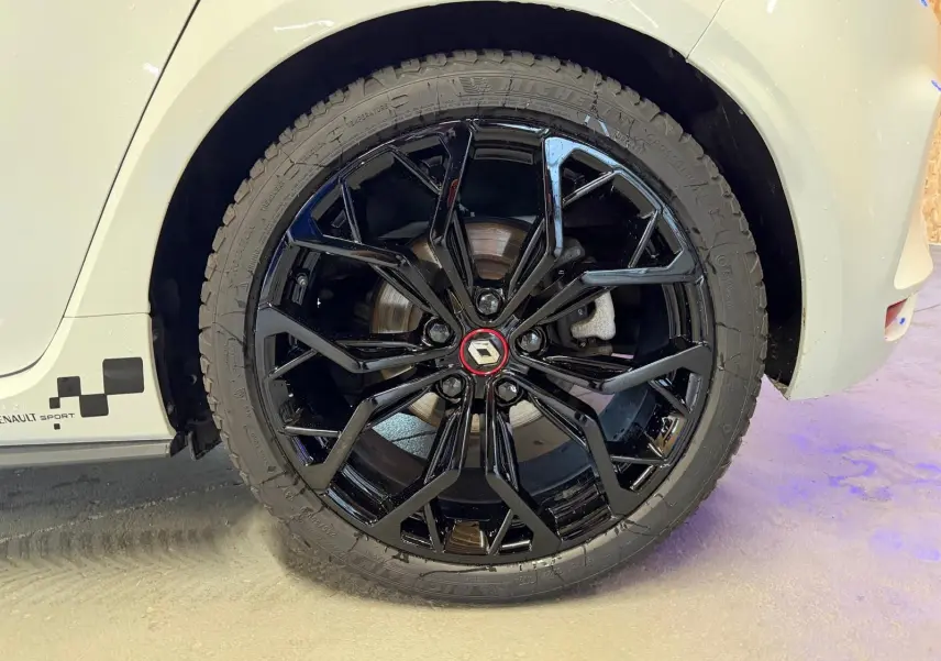 Gros plan sur la roue arrière droite noire brillante d'une Renault Mégane IV RS 280 blanche avec logo Renault rouge.