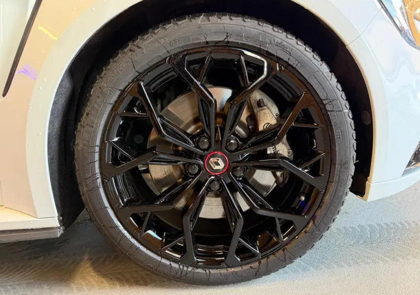 Gros plan sur la roue avant droite noire brillante avec logo Renault, sur une Renault Mégane IV RS 280 blanche.