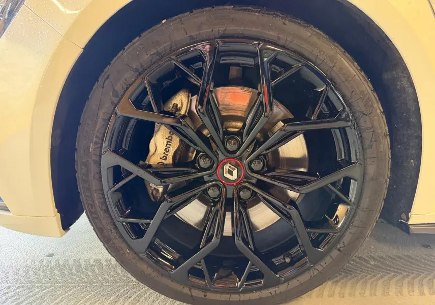 Gros plan sur la jante noire brillante de la Renault Mégane IV RS 280 EDC6 blanche avec logo Renault au centre.