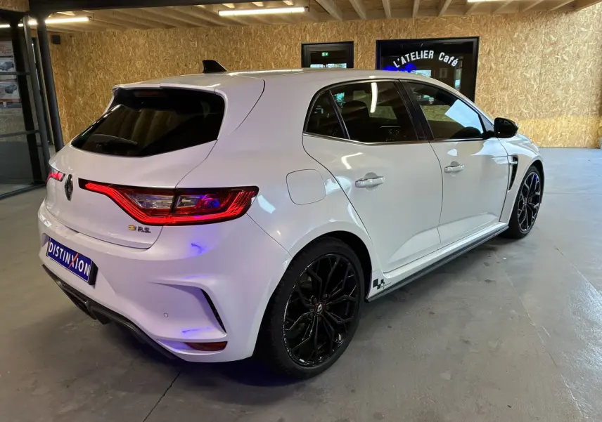 Vue 3/4 arrière droite d'une Renault Mégane IV RS 280 EDC6 blanche avec jantes noires et vitres teintées dans un garage.
