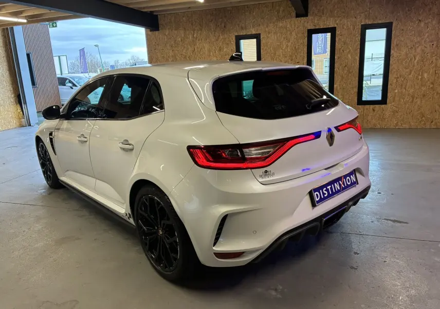 Vue 3/4 arrière droite d'une Renault Mégane IV RS 280 EDC6 blanche avec jantes noires dans un garage.