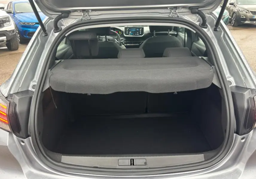 Vue arrière du coffre ouvert d'une Peugeot 208 Hybrid gris 2025, avec tablette cache-bagages et intérieur visible.