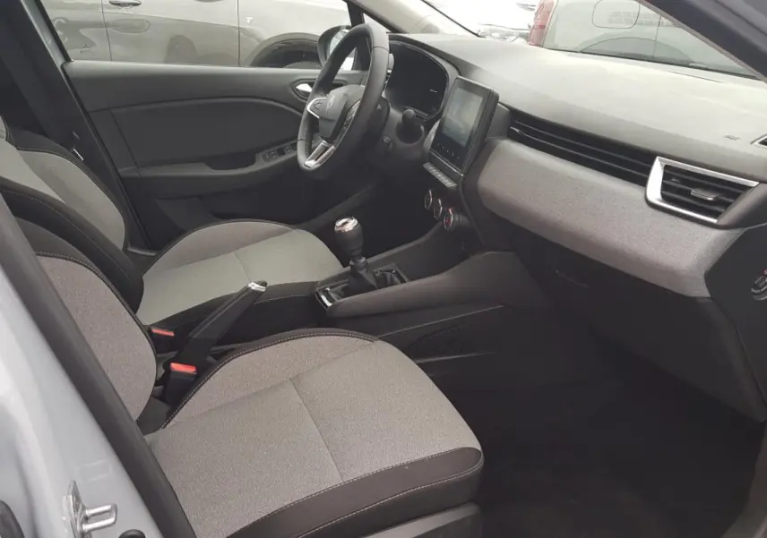 Vue intérieure côté conducteur de la Renault Clio gris 2025, montrant sièges tissu, tableau de bord et levier de vitesse manuel.