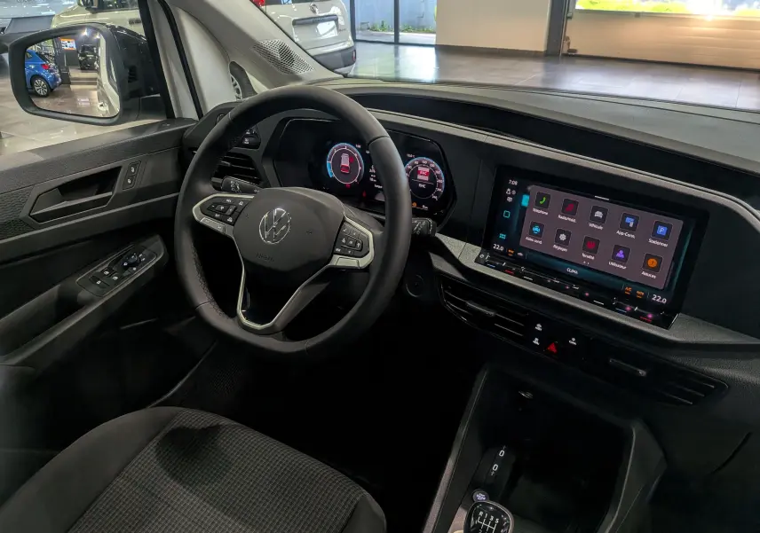 Vue intérieure côté conducteur du Volkswagen Caddy blanc 2025, avec tableau de bord numérique et écran tactile central.