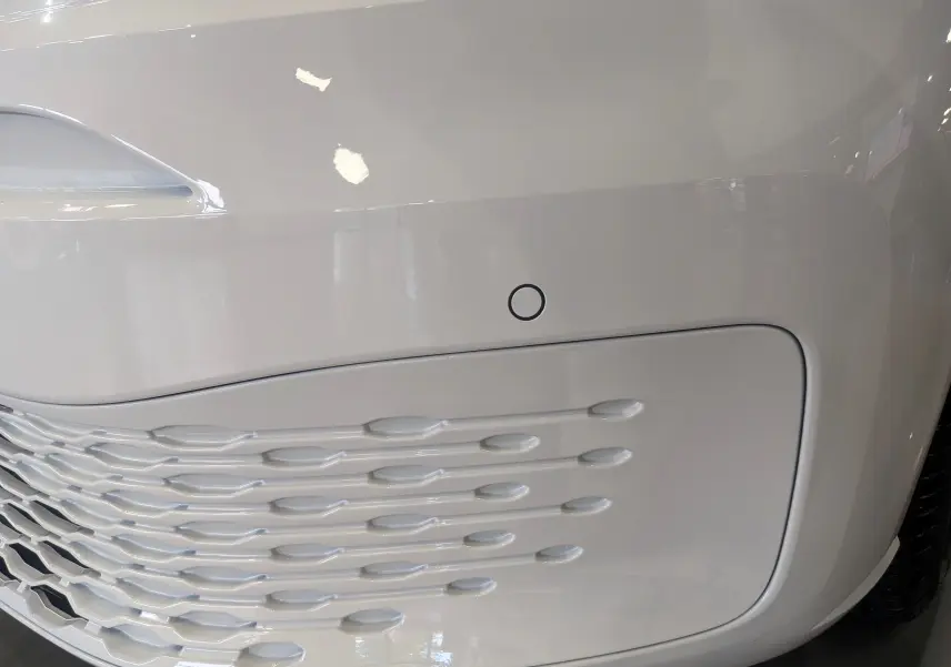 Détail du pare-chocs avant blanc du Volkswagen Caddy 2.0 TDI 102 CH 2025 avec capteur de stationnement intégré.