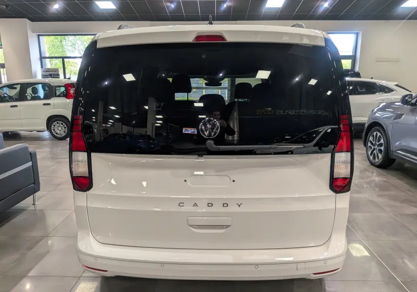 Vue arrière d'un Volkswagen Caddy blanc 2025 avec vitres arrière teintées et logo VW visible au centre.