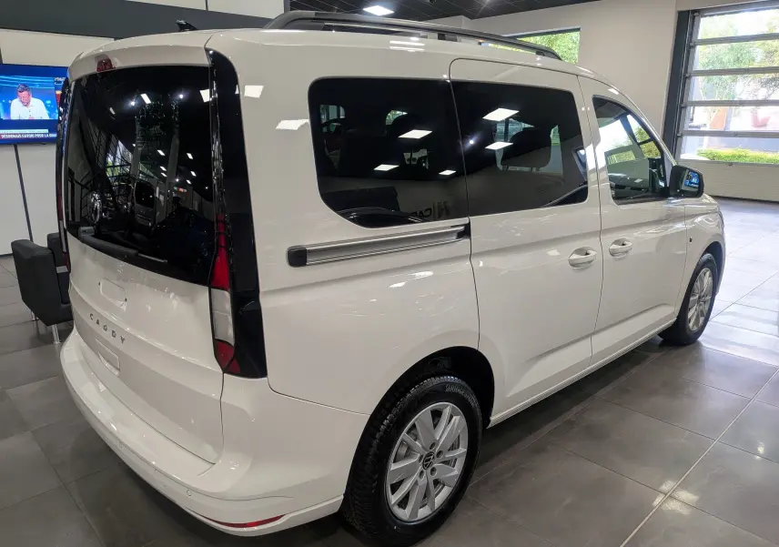 Vue 3/4 arrière droite d'un Volkswagen Caddy blanc 2025 avec vitres teintées et jantes alliage en showroom.
