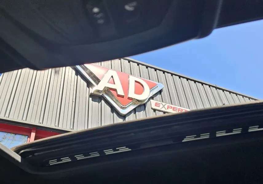 Toit ouvrant panoramique ouvert d'une BMW X4 xDrive20dA noire, vue vers le ciel et une enseigne AD Expert.