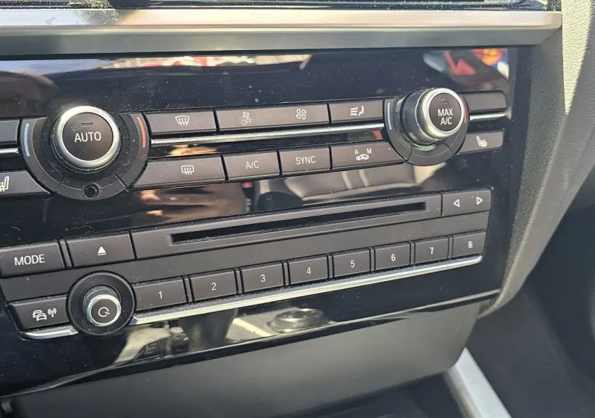 Gros plan sur la console centrale noire du BMW X4 xDrive20dA 2015, mettant en valeur les commandes de climatisation et audio.