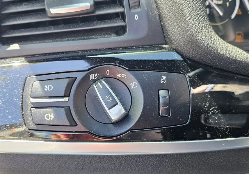 Gros plan sur le bouton de commande des phares sur tableau de bord noir brillant d'une BMW X4 xDrive20dA 2015.