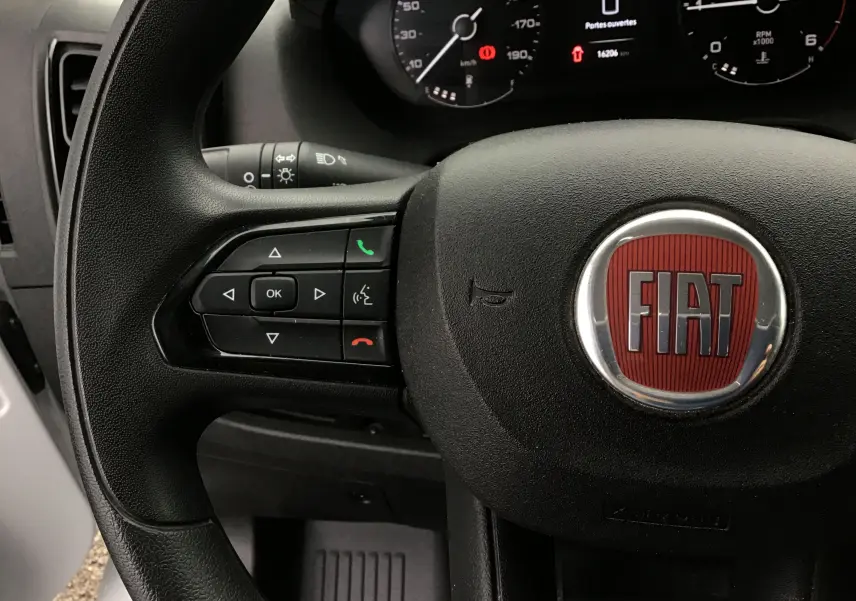 Gros plan sur le volant noir du Fiat Ducato Fourgon 2024 avec logo rouge et commandes intégrées côté gauche.