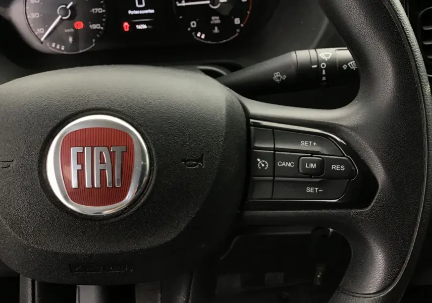 Gros plan sur le volant noir du Fiat Ducato Fourgon 2024 avec commandes de régulateur et logo rouge FIAT central.