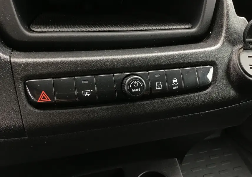 Gros plan sur la rangée de boutons noirs du tableau de bord du Fiat Ducato Fourgon blanc, avec commande mute au centre.