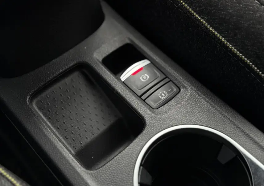 Gros plan sur la console centrale du Renault Captur 2025, montrant le frein à main électrique et un espace de rangement noir.