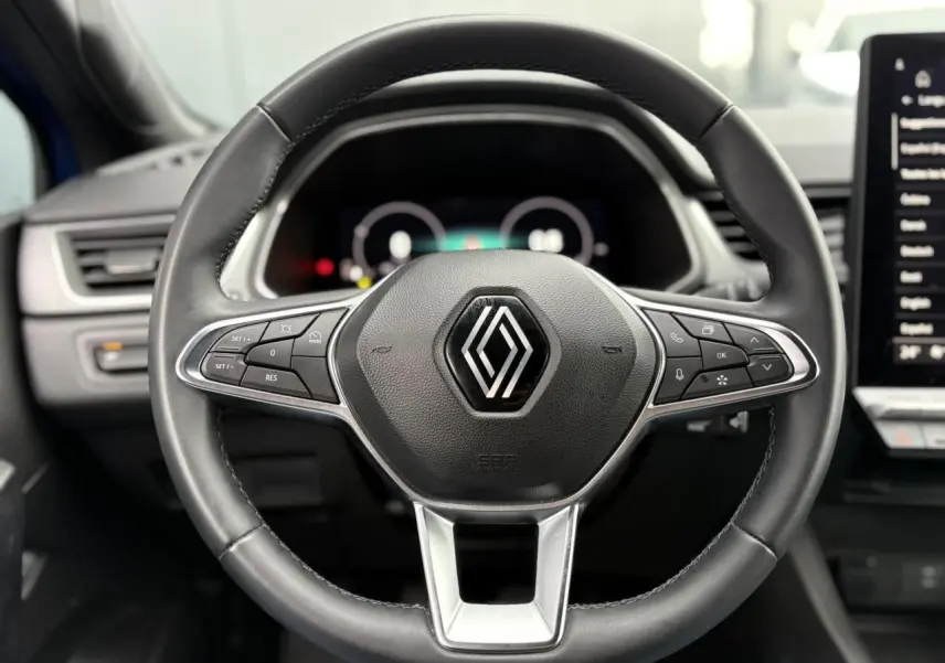 Vue centrée sur le volant cuir noir du Renault Captur 2025 avec commandes intégrées et tableau de bord numérique flou.