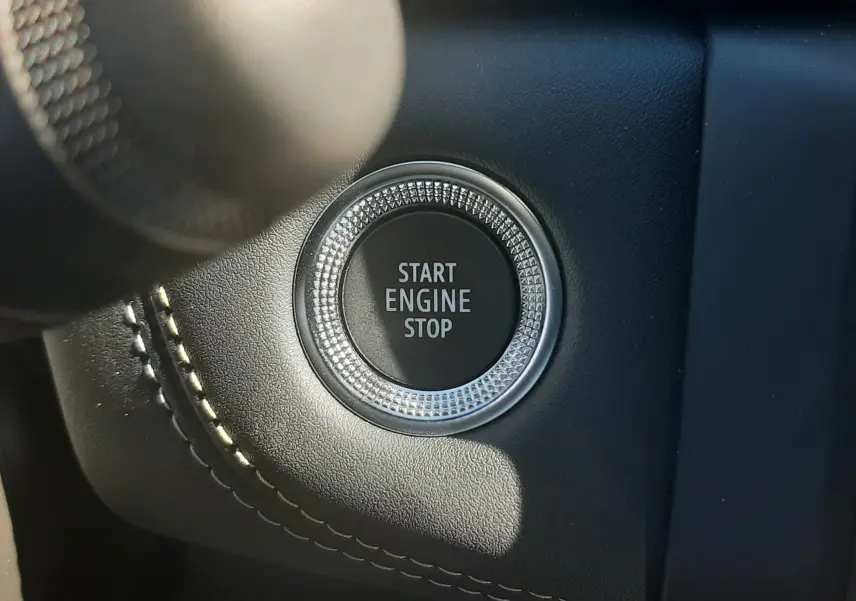Gros plan sur le bouton Start Engine Stop entouré de cuir noir avec surpiqûres dans l'habitacle du Renault Symbioz gris cassiopée.