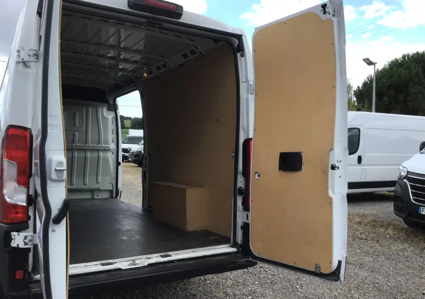 Vue arrière ouverte du FIAT Ducato Fourgon blanc 2024, montrant l'intérieur vide avec parois en bois et porte battante ouverte.