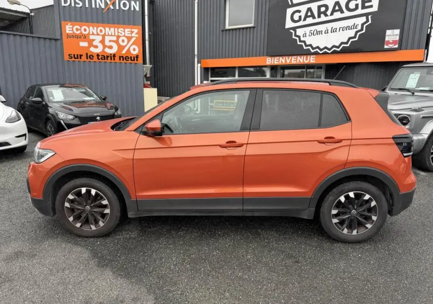 Profil droit d'un Volkswagen T-Cross 1.0 TSI 110 Active orange métallisé avec jantes Galway 16 pouces sur parking.