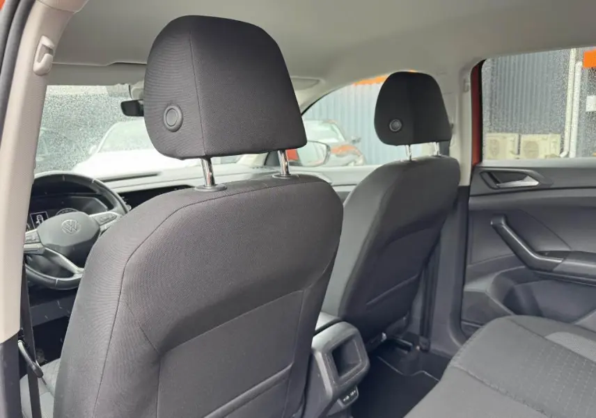 Vue intérieure arrière du Volkswagen T-Cross orange 2021, montrant les sièges avant en tissu noir et la console centrale.