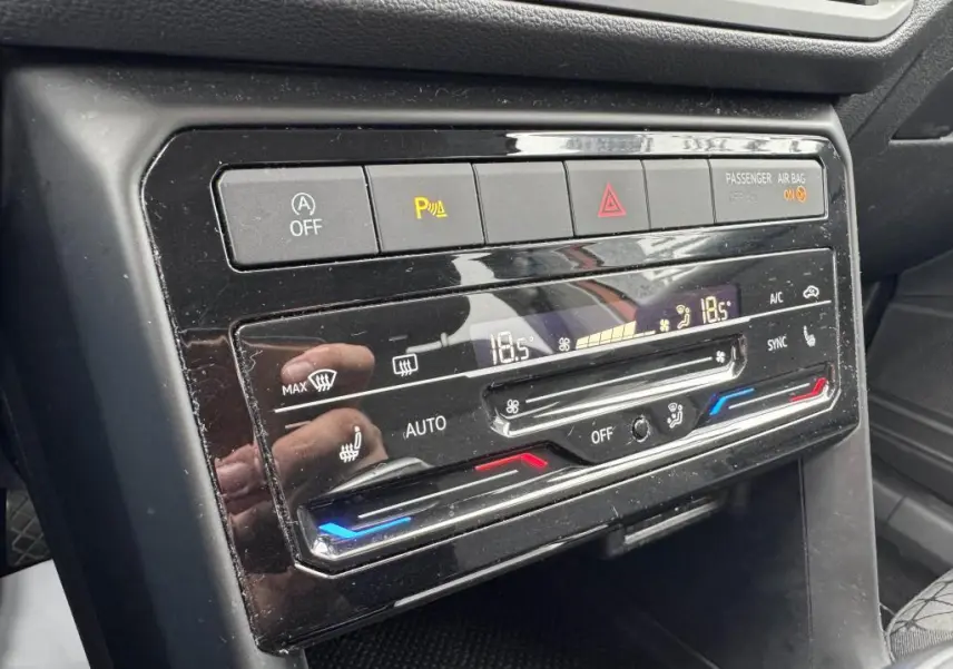 Gros plan sur la console centrale noire du Volkswagen T-cross 1.0 TSI Active, montrant les commandes de climatisation digitale et alertes.