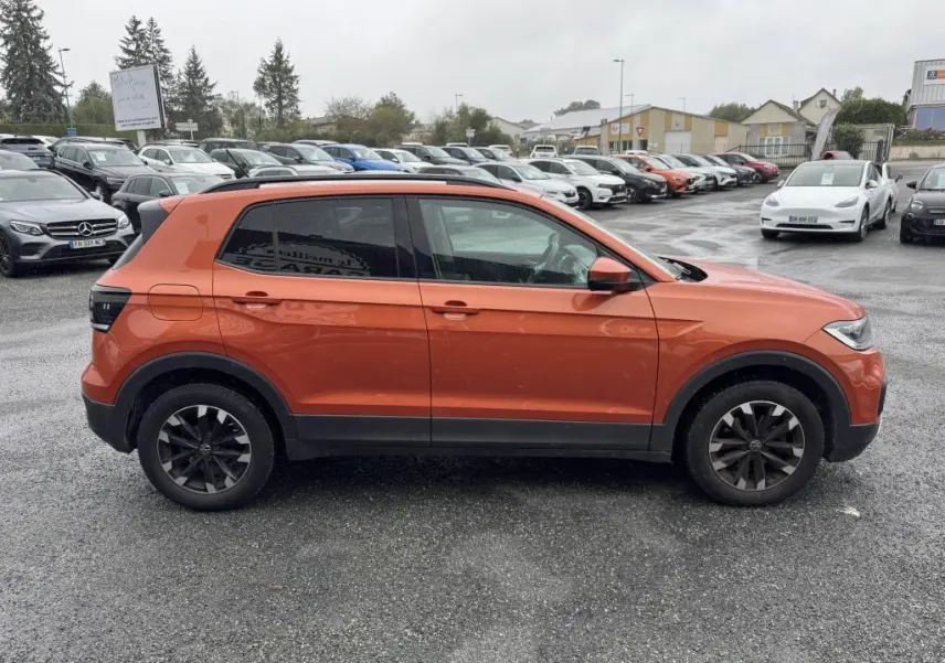 Profil côté gauche d'un Volkswagen T-Cross orange métallisé 2021 avec jantes Galway noires sur parking humide.
