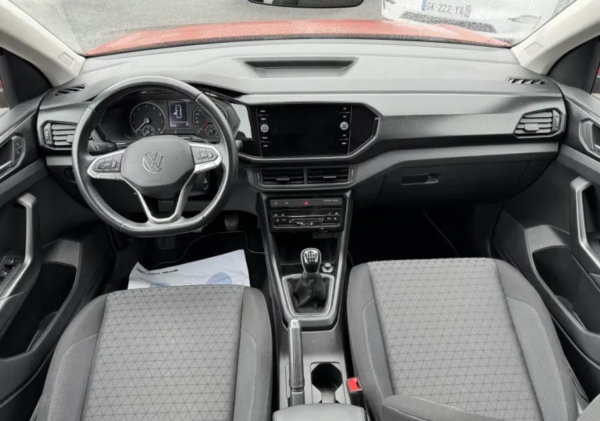 Vue intérieure avant du Volkswagen T-Cross 1.0 TSI 110 Active 2021, tableau de bord noir avec volant cuir et levier de vitesses manuel.