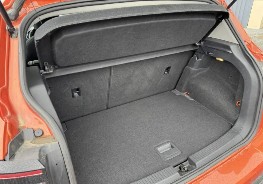 Coffre ouvert vu de l'arrière du Volkswagen T-Cross orange métallisé, montrant l'espace de chargement et la plage arrière.