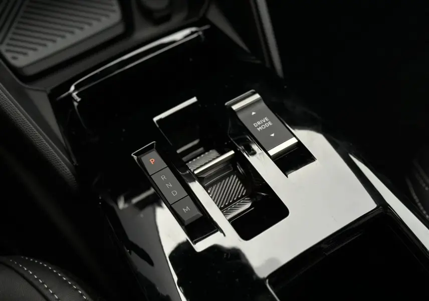 Gros plan sur la console centrale noire brillante de la Citroën C4 NV Hybrid 145 e-DSC6 Max avec sélecteur de vitesse et bouton Drive Mode.