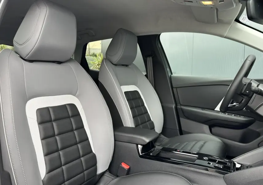 Vue intérieure côté conducteur de la Citroën C4 2025 avec sièges Advanced Comfort gris clair et noir à motifs carrés.