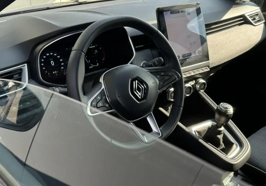Vue intérieure du poste de conduite de la Renault Clio TCE 90 Techno 2025 avec volant multifonction et écran tactile vertical.