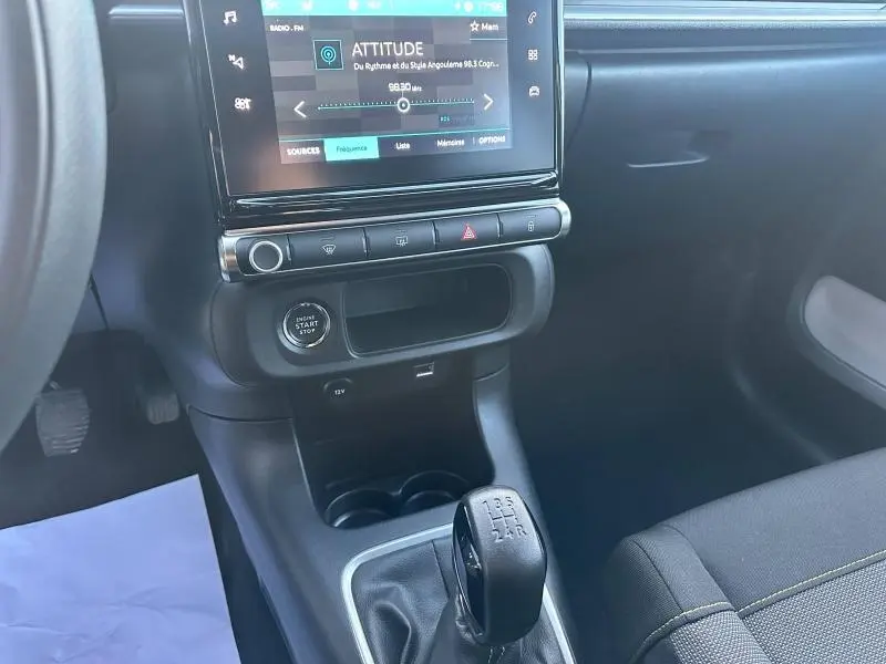 Vue intérieure centrée sur la console centrale d'une Citroën C3 grise 2023, avec écran tactile et levier de vitesse manuel.