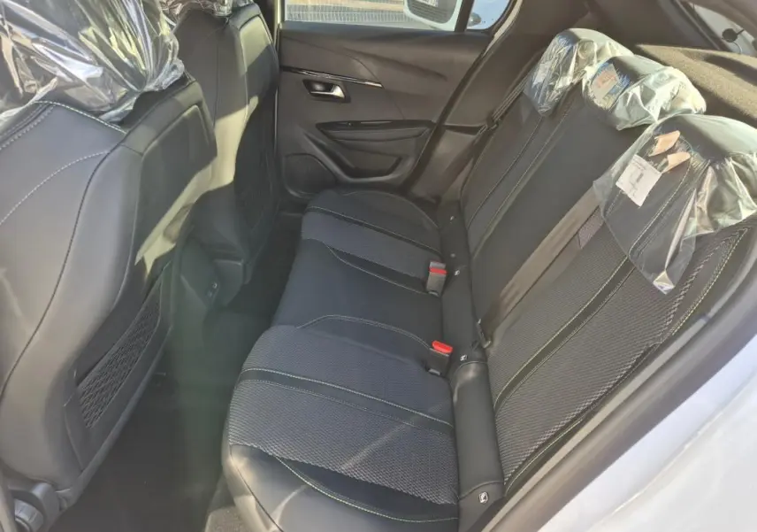 Vue intérieure arrière côté droit montrant les sièges noirs avec surpiqûres vertes d'une Peugeot 208 Hybrid 136 e-DCS6 GT blanche.