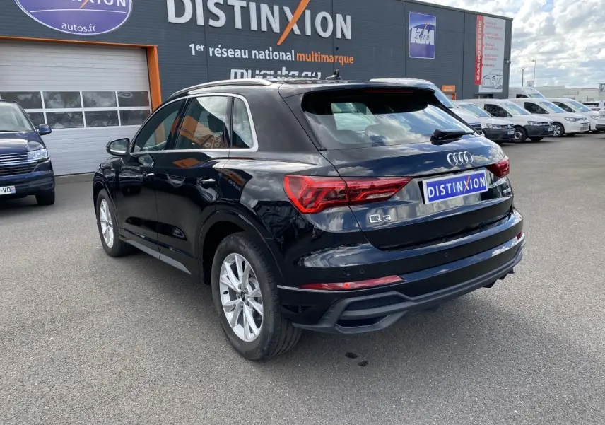Audi Q3 noir intense métallisé vue 3/4 arrière droit, avec jantes aluminium et logo S line sur ailes avant.