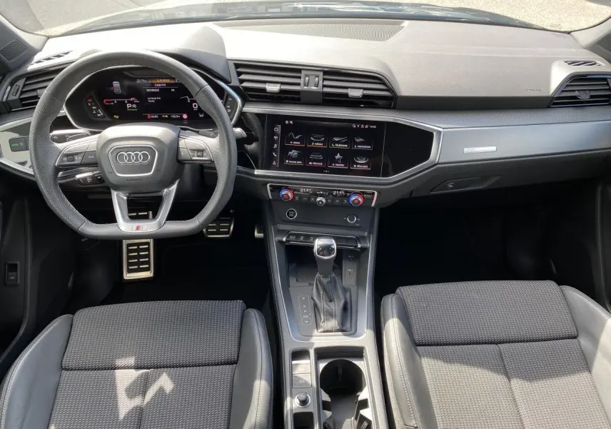 Vue intérieure avant de l'Audi Q3 2024 avec tableau de bord noir, volant cuir S line et console centrale moderne.