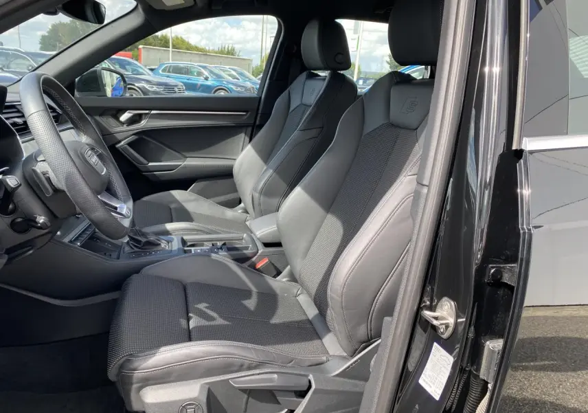 Vue intérieure côté conducteur de l'Audi Q3 S line 2024 avec sièges sport noirs et volant cuir multifonction.