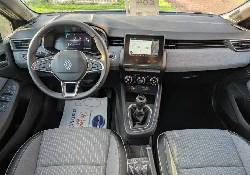 Vue intérieure avant de la Renault Clio 2025, tableau de bord gris avec volant multifonction et levier de vitesses manuel.