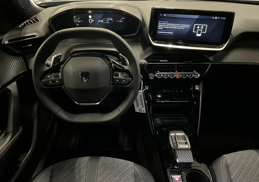 Vue intérieure frontale du tableau de bord et volant noir du Peugeot 2008 1.2 Hybrid 145ch Allure, avec écran tactile et finitions carbone.