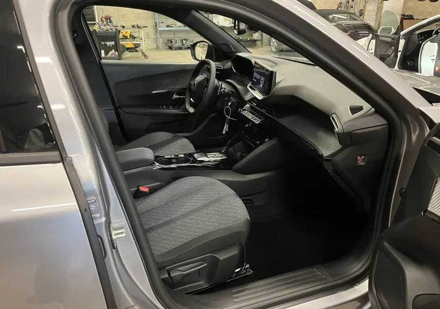 Vue intérieure côté conducteur du Peugeot 2008 gris Artense 2025, montrant le tableau de bord moderne et les sièges tissu gris.