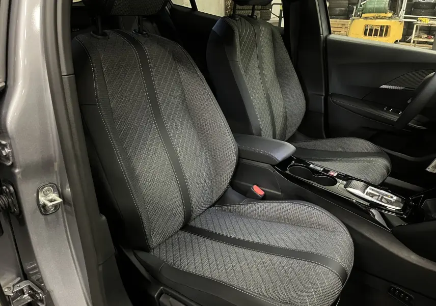 Vue intérieure côté conducteur du Peugeot 2008 gris Artense, sièges tissu gris avec surpiqûres et console centrale brillante.