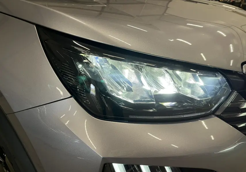 Gros plan sur le phare avant droit du Peugeot 2008 gris Artense métal, mettant en valeur ses lignes modernes et LED.