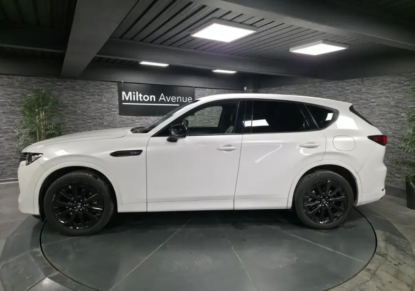 Vue de profil côté gauche du Mazda CX-60 blanc Arctic White avec jantes alliage noires dans un showroom.