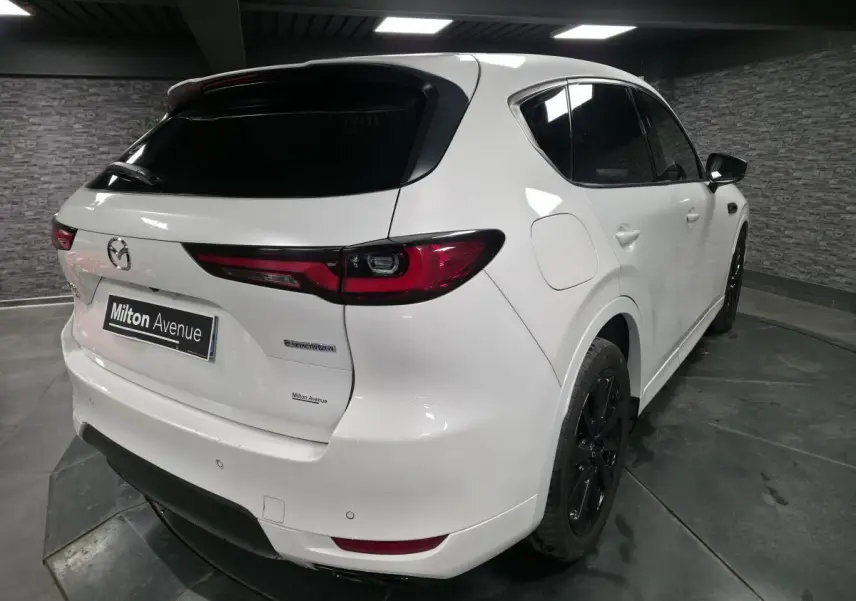 Vue 3/4 arrière droit du Mazda CX-60 blanc avec jantes noires et feux arrière LED dans un garage.