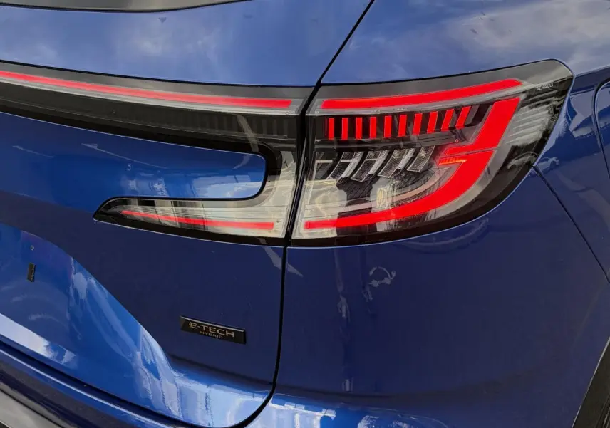 Gros plan sur le feu arrière droit rouge et noir du Renault Austral Bleu Iron avec logo E-Tech Hybrid visible.
