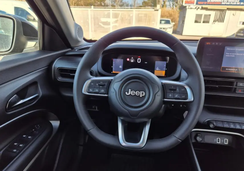 Vue intérieure centrée sur le volant Jeep noir avec tableau de bord numérique et écran tactile à droite.