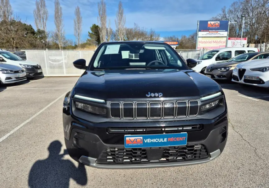Vue avant d'un Jeep Avenger noir 2024 avec calandre distinctive et phares LED fins, sur parking extérieur.
