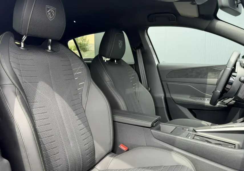 Vue intérieure côté gauche des sièges avant noirs avec surpiqûres vert Adamite et blason Peugeot embossé sur appuie-têtes.