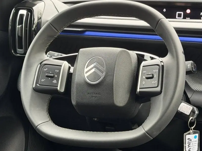 Vue rapprochée du volant noir de la Citroën C3 1.2 Turbo 100ch PLUS 2025 avec commandes intégrées et bandeau bleu au tableau de bord.